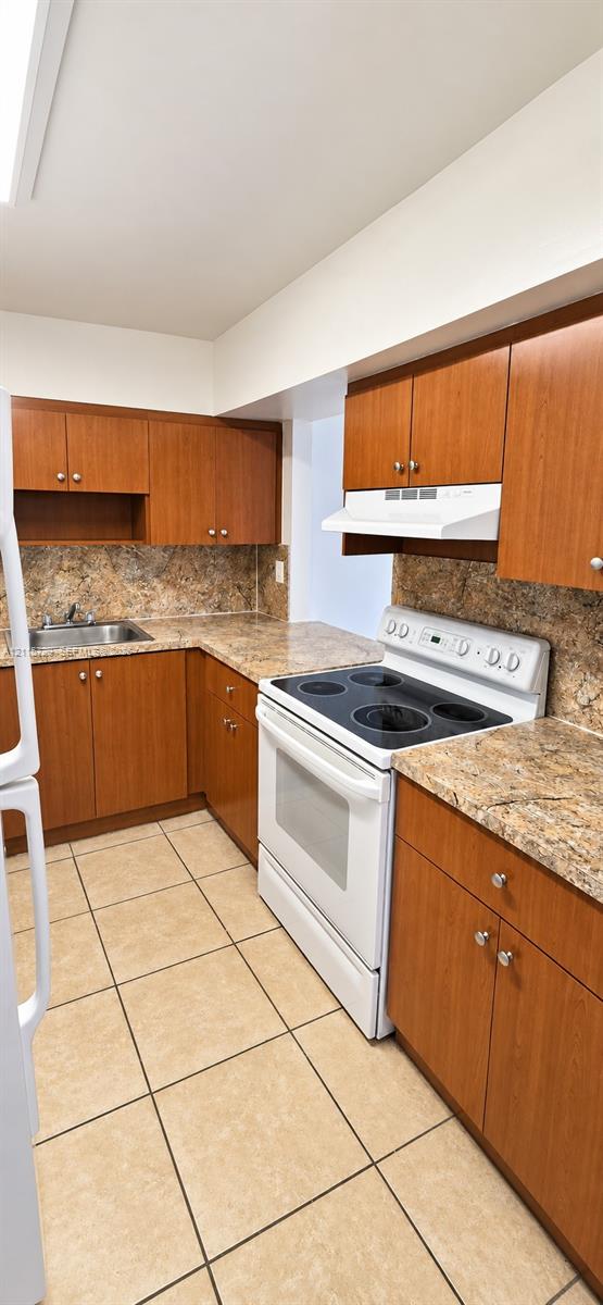 Kitchen featuring wood cabinetry, stone-finish countertops, tile flooring, and integrated white appliances