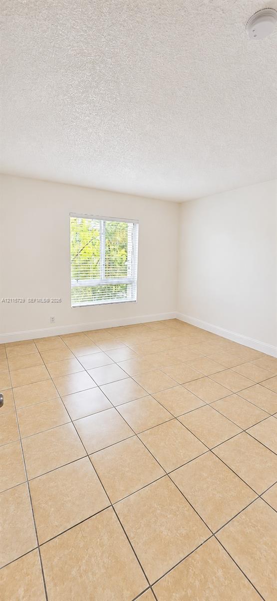 Interior room featuring large-format neutral floor tiling, a single-hung window with horizontal blinds, and a textured ceiling finish
