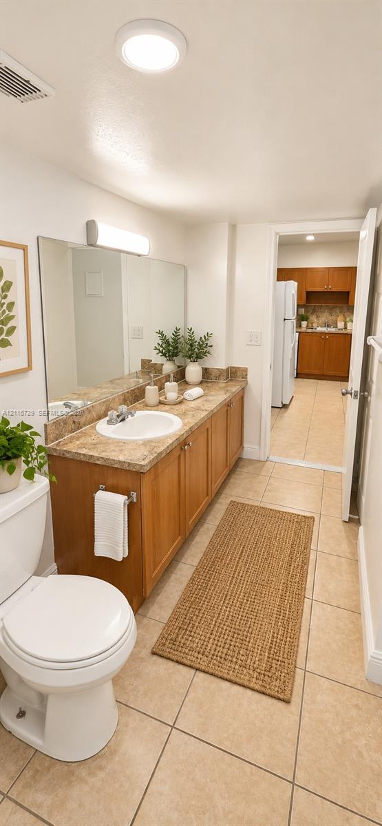Bathroom featuring a wood-toned vanity cabinet, stone-finish countertop with an integrated basin, wall-to-wall mirror, and ceramic tile flooring