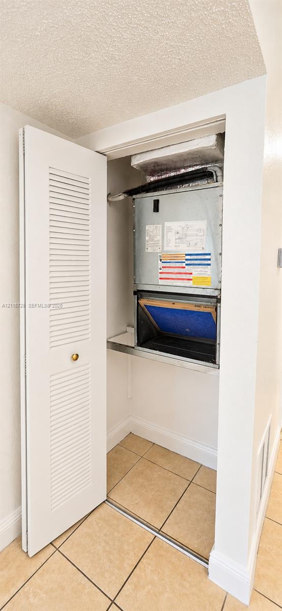 Wall-mounted HVAC air handler unit with a louvered bi-fold closet door and ceramic tile flooring Wall-mounted HVAC air handler unit with a louvered bi-fold closet door and ceramic tile flooring