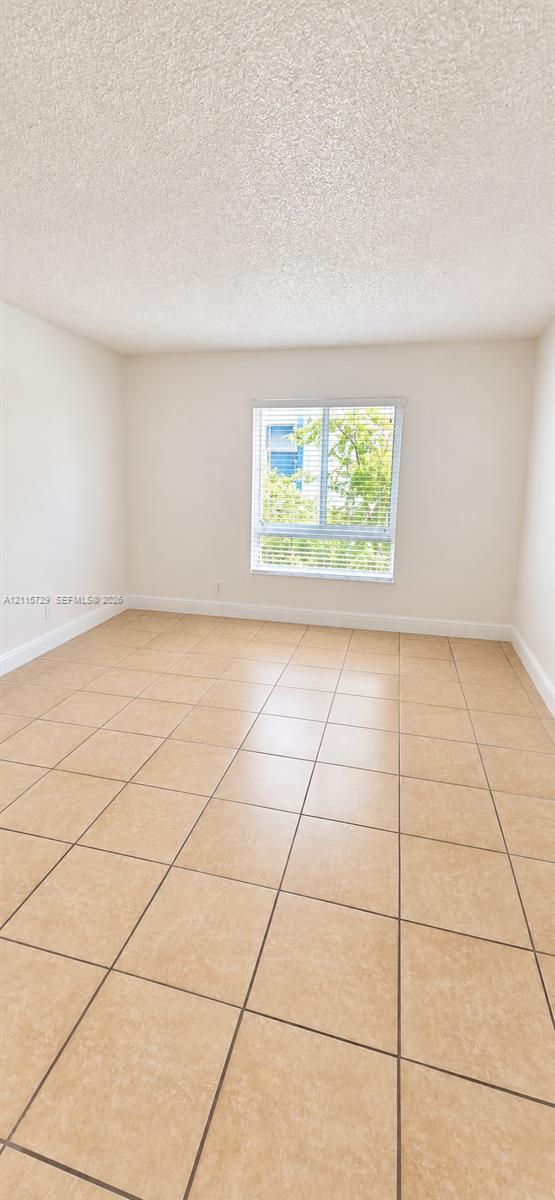 Interior space featuring neutral-toned tile flooring, light-colored walls, textured ceiling, and a single window with horizontal blinds