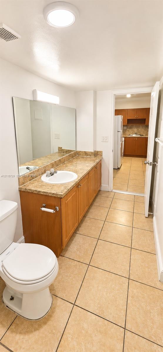 Bathroom featuring a long wood-finish vanity with a stone-finish countertop, integrated oval sink, full-width wall mirror, and neutral tile flooring