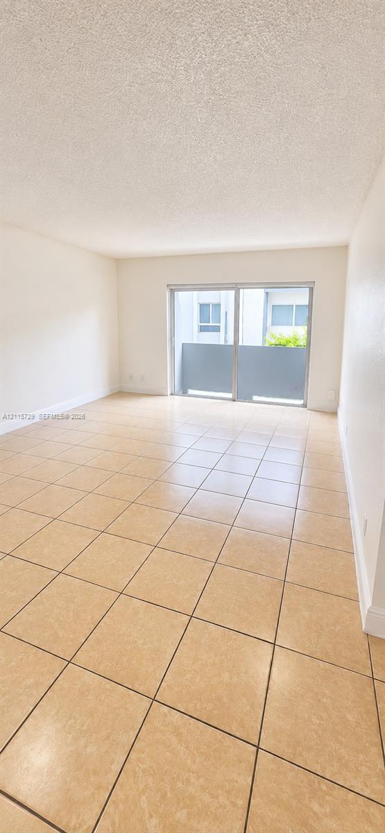 Interior living space featuring large-format square tile flooring, neutral walls, and a sliding glass door providing external access to a private balcony Interior living space featuring large-format square tile flooring, neutral walls, and a sliding glass door providing external access to a private balcony