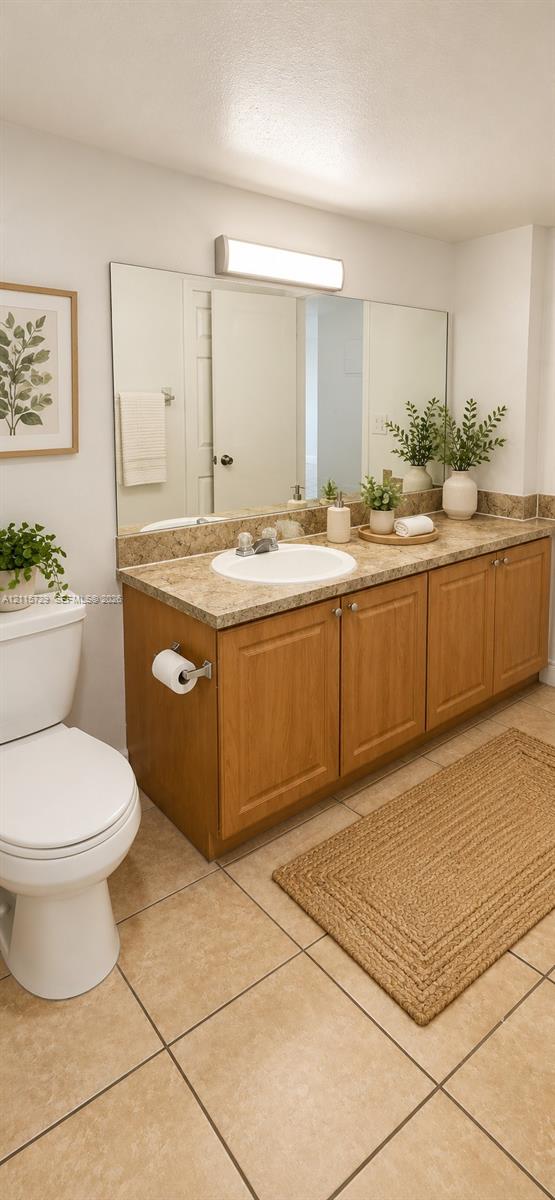 Bathroom vanity featuring wood-finish cabinetry, a stone-composite countertop with an integrated basin, large wall-mounted mirror, and ceramic tile flooring