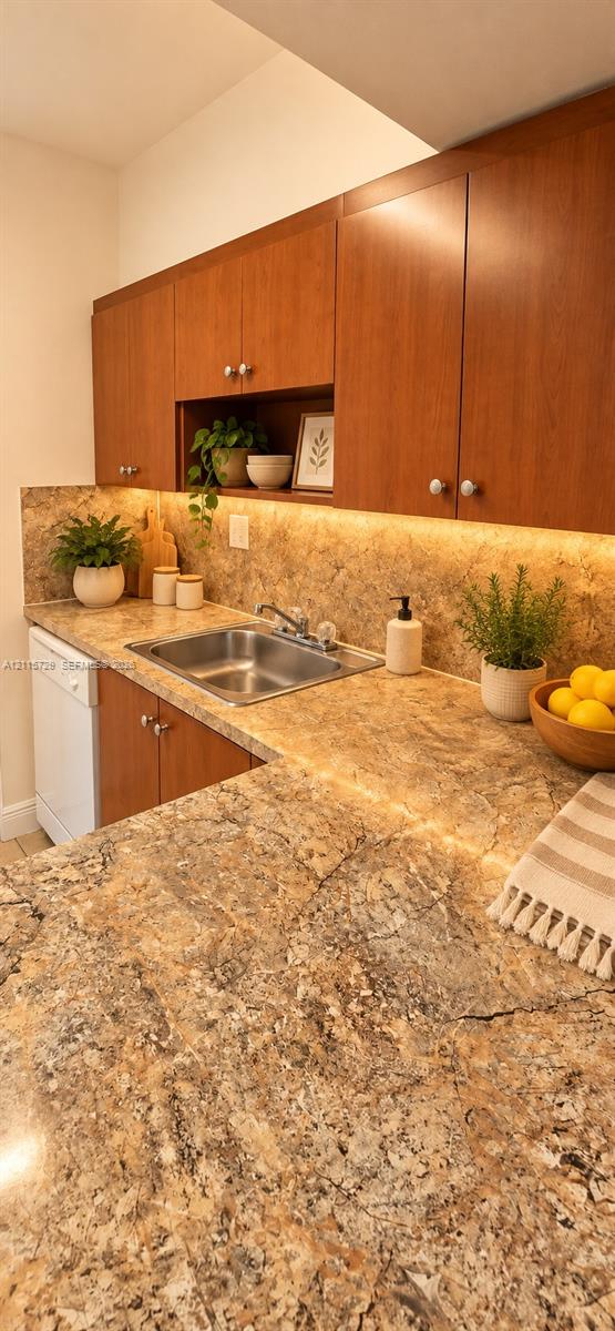 Kitchen featuring wood cabinetry, stone-finish countertops, an integrated under-cabinet lighting system, a stainless steel sink with a dual-handle faucet, and an open display niche