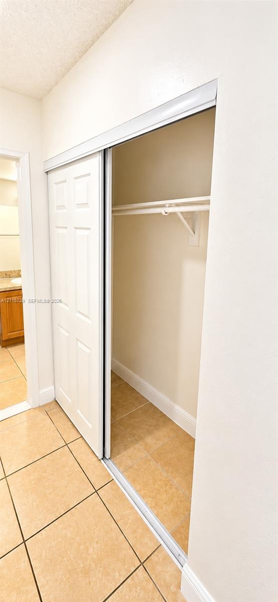Closet featuring white six-panel sliding doors, a white overhead hanging rod, and tile flooring
