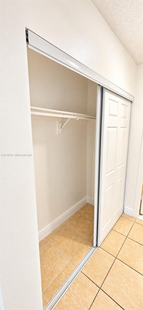 Closet featuring sliding six-panel doors, a built-in hanging rod, a high-mounted shelf, and ceramic tile flooring