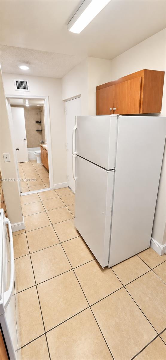 Ceramic tile flooring, white top-mount refrigerator, wood-finish upper cabinetry, and flush-mount ceiling lighting