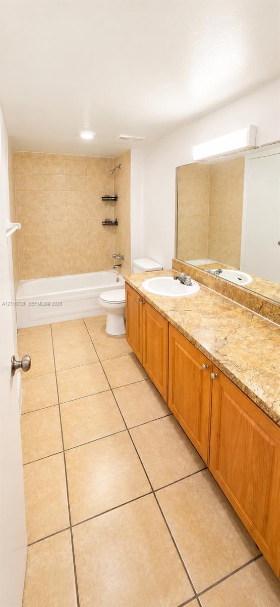 Bathroom featuring a vanity with a stone-finish countertop, undermount sink, ceramic tile flooring, and a shower-tub combination with tiled walls