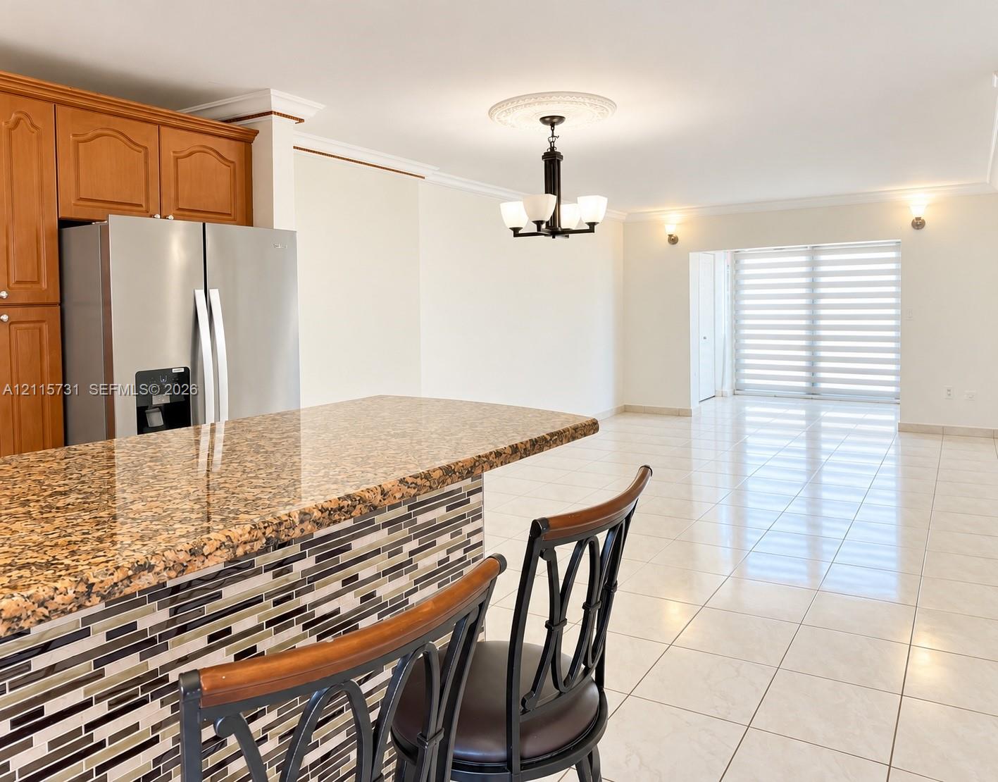 Kitchen island featuring stone countertop and decorative multi-toned tile base, wood-finish cabinetry, stainless steel refrigerator, and tiled flooring Kitchen island featuring stone countertop and decorative multi-toned tile base, wood-finish cabinetry, stainless steel refrigerator, and tiled flooring