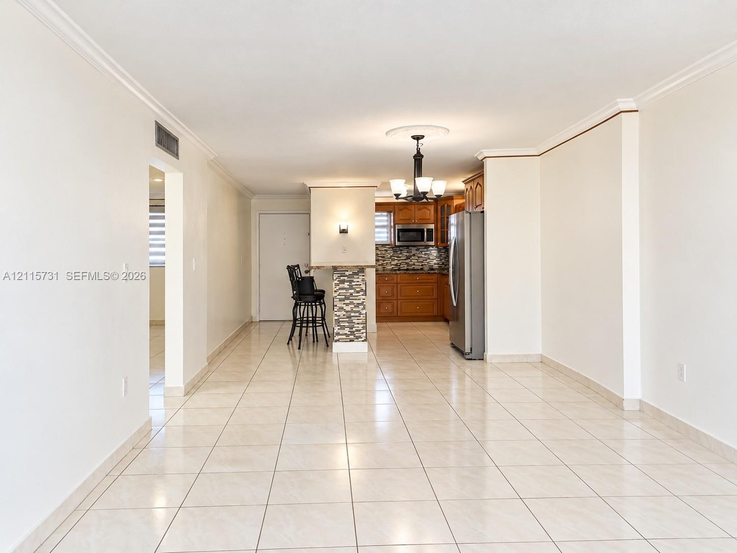 Open-concept interior featuring neutral tile flooring, built-in breakfast bar with stone-finish cladding, wood-finish cabinetry, and crown molding
