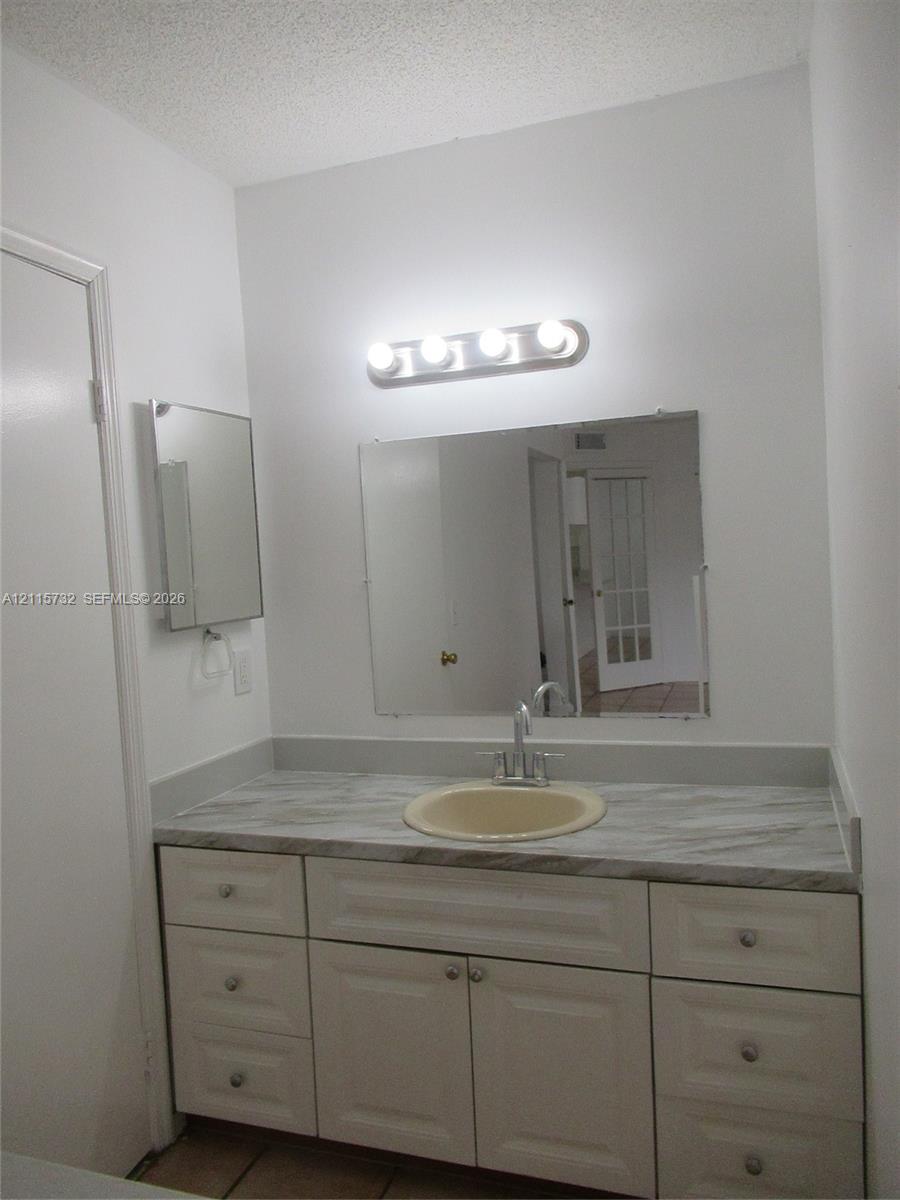 Vanity featuring white raised-panel cabinetry, a stone-patterned laminate countertop, an integrated oval basin with a dual-handle faucet, and an oversized wall-mounted mirror with a four-light fixture