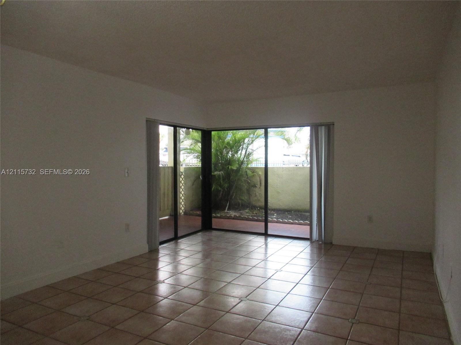 Interior space featuring neutral-toned tile flooring and expansive sliding glass corner doors opening to an enclosed patio area
