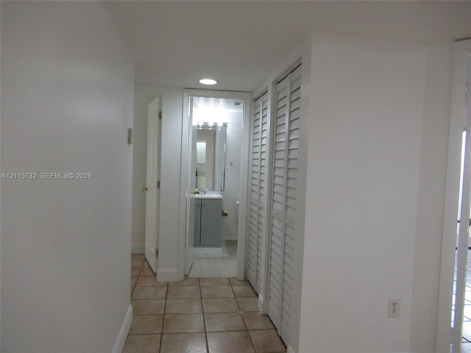 Neutral-toned ceramic floor tile with white louvered-style bi-fold closet doors and recessed ceiling lighting