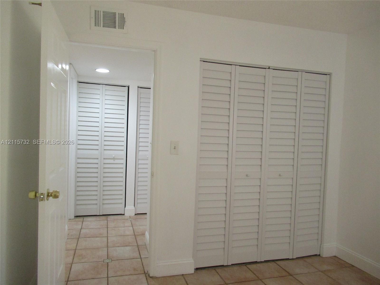 Interior space featuring white louvered bifold closet doors and neutral-toned ceramic tile flooring