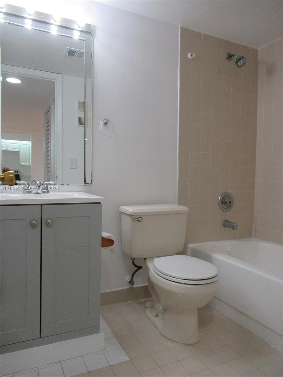 Bathroom featuring a gray vanity with an integrated sink, a rectangular mirror with integrated lighting, and a bathtub with tile surround