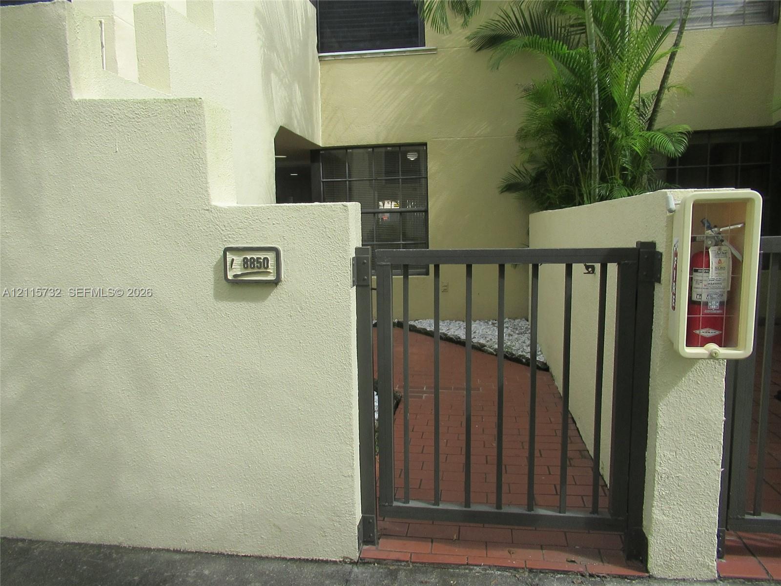 Stucco exterior facade featuring a gated entrance, red brick walkway, and structured stone accents Stucco exterior facade featuring a gated entrance, red brick walkway, and structured stone accents