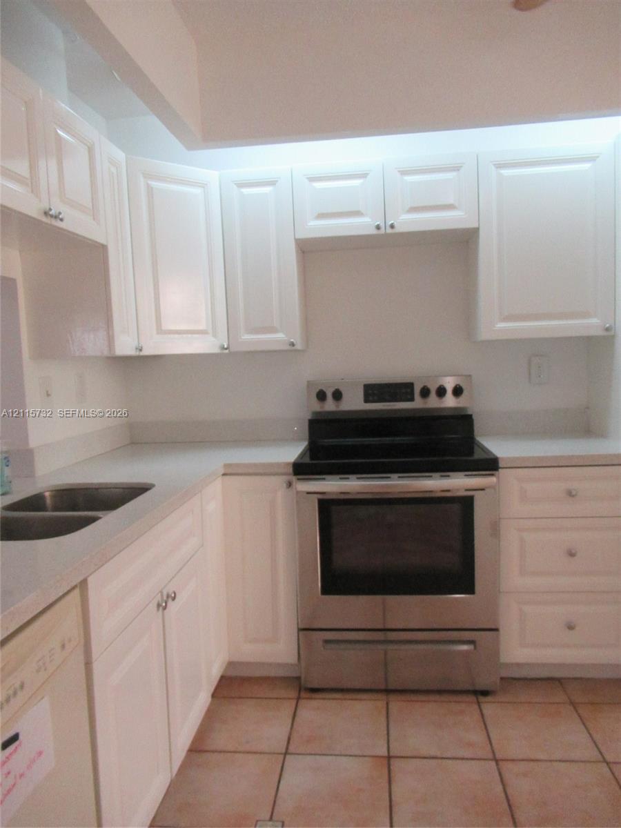 Kitchen featuring white shaker-style cabinetry, solid-surface countertops, dual-basin stainless steel sink, stainless steel range, and tile flooring Kitchen featuring white shaker-style cabinetry, solid-surface countertops, dual-basin stainless steel sink, stainless steel range, and tile flooring