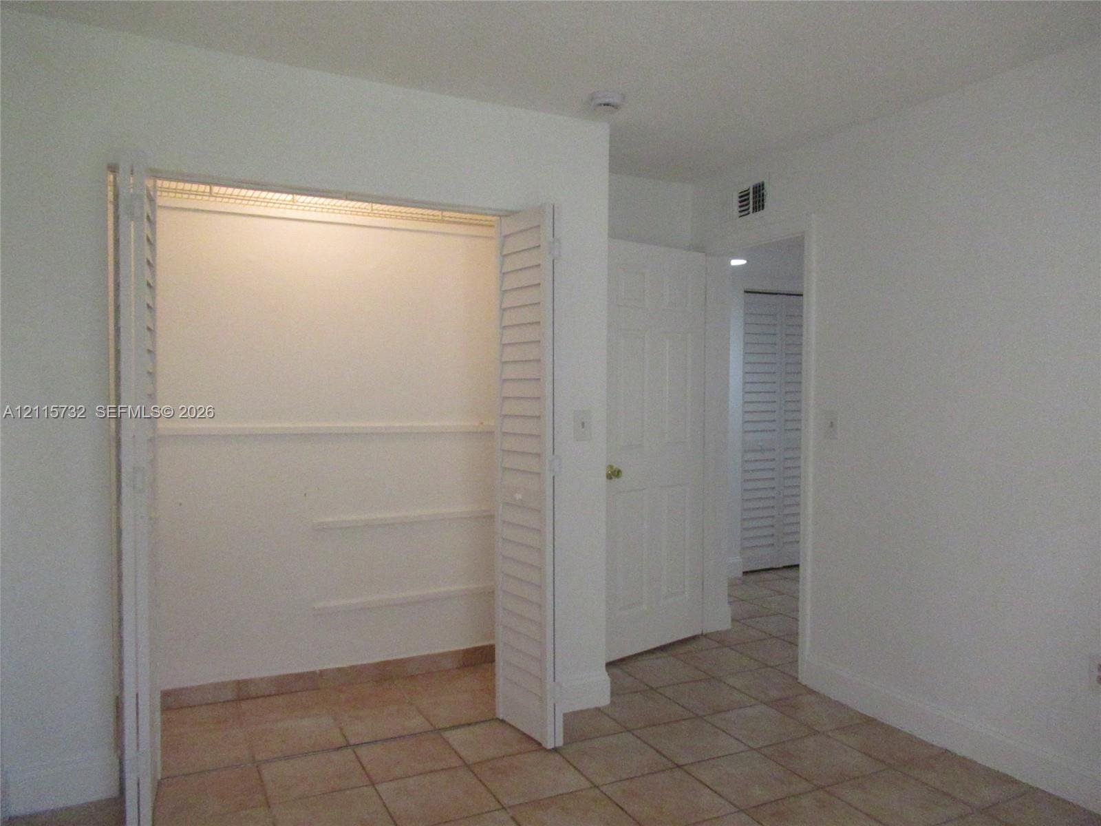 Closet with louvered bi-fold doors, white interior shelving, solid-core six-panel door, and neutral tile flooring