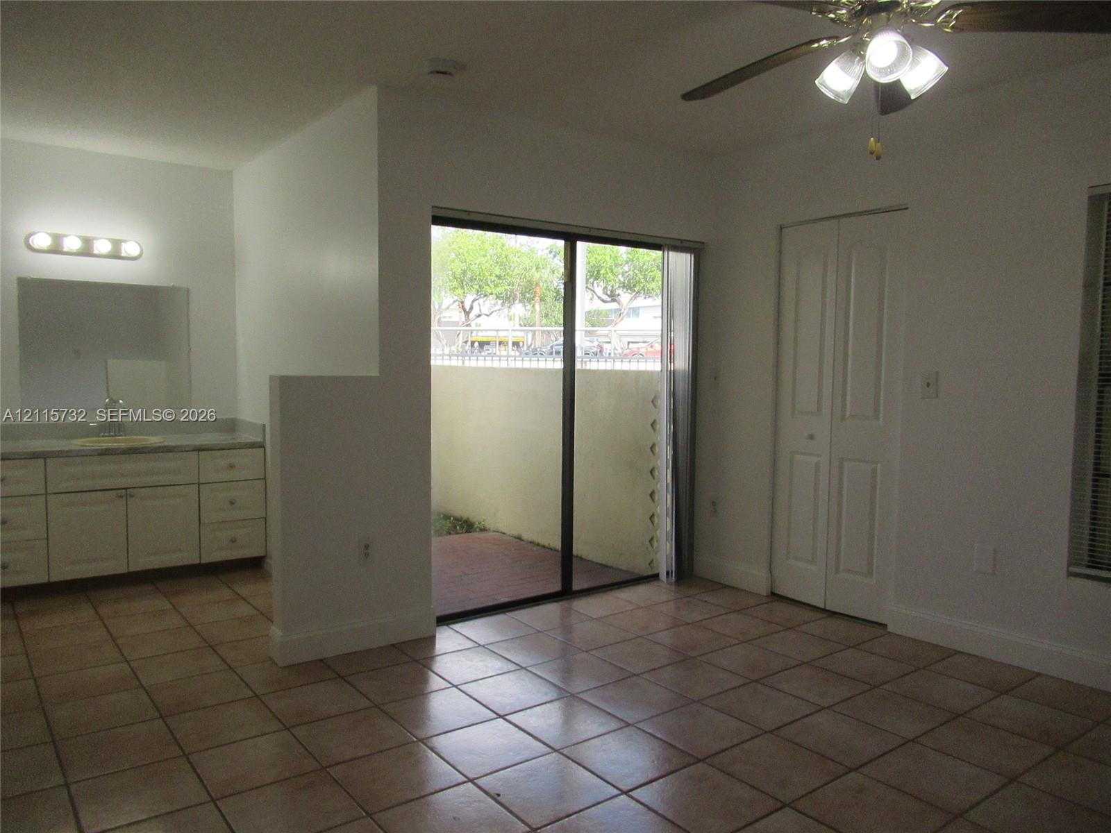 Ceramic tile flooring, vanity with stone-finish countertop, ceiling fan with light fixture, sliding glass door, and bi-fold closet doors