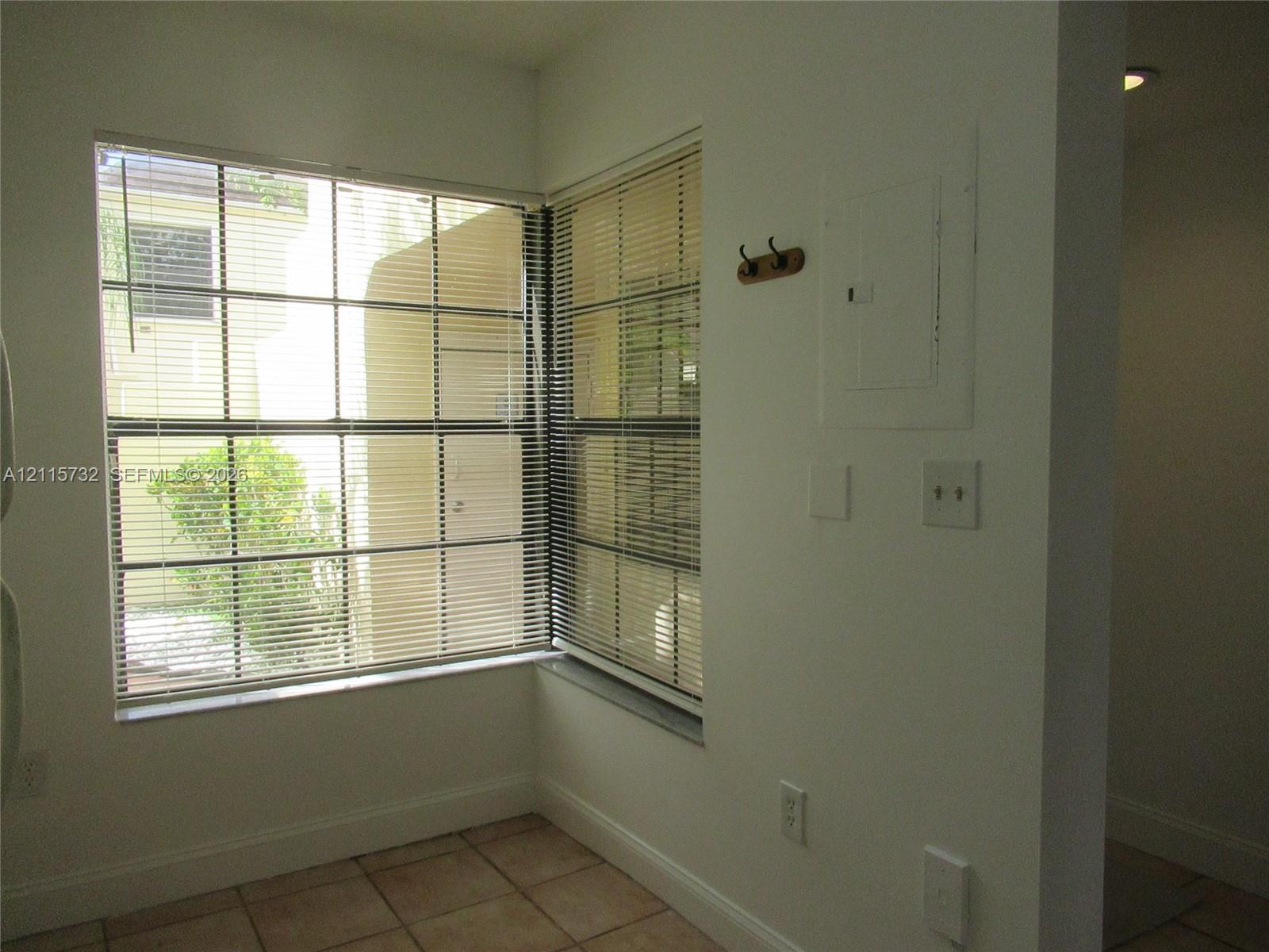 Corner window configuration with horizontal blinds, tile flooring, and a wall-mounted wood hook fixture