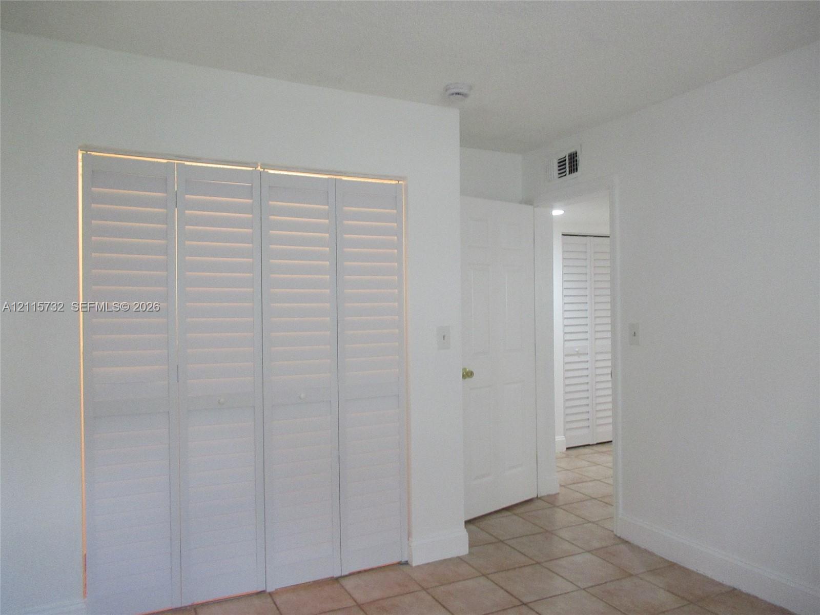 White louvered bifold closet doors, interior six-panel door, and neutral tile flooring