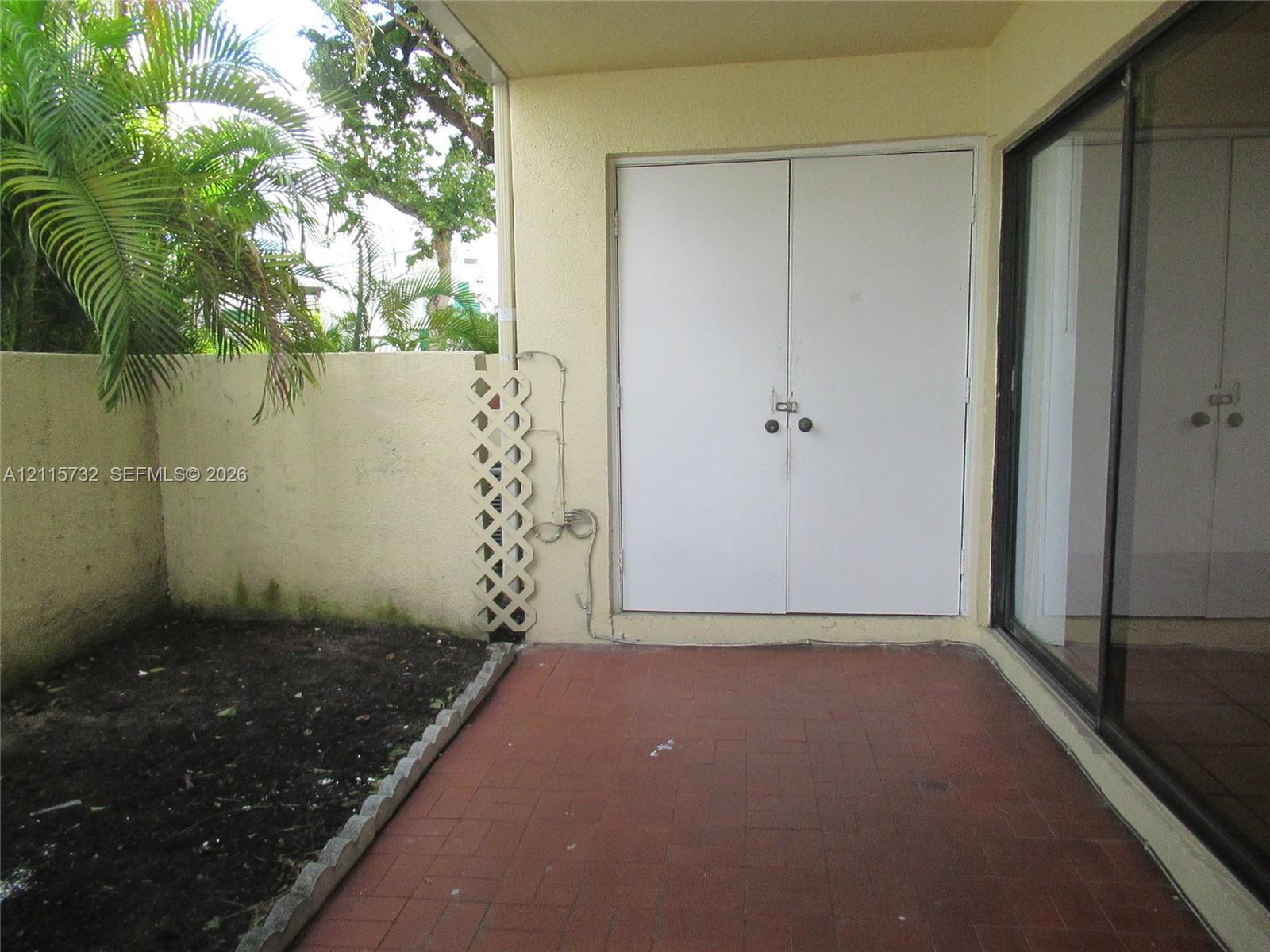 Covered patio featuring red tile flooring, double-door storage access, and a walled perimeter with decorative lattice screening