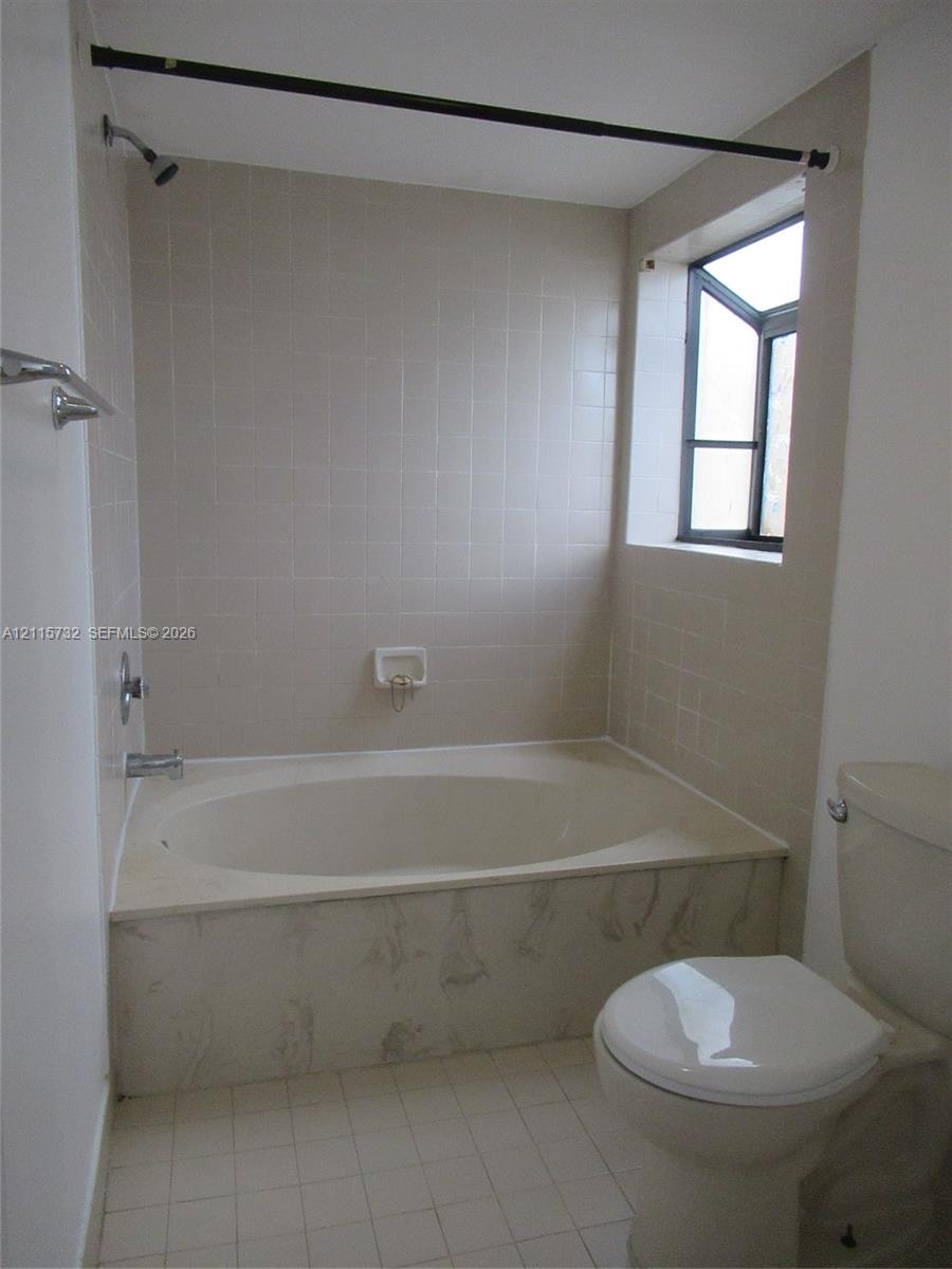 Full-size soaking tub featuring a tiled surround, neutral ceramic wall tiling, a casement window, and wall-mounted shower fixture