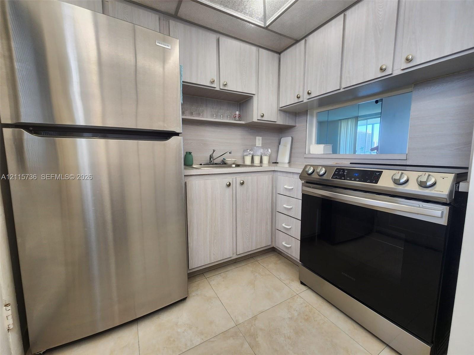 Kitchen featuring stainless steel refrigerator, slide-in electric range, light-toned cabinetry, light-toned solid surface countertops, and tile flooring
