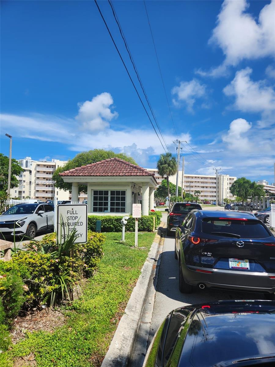 Gated community entrance featuring a guardhouse with a tiled roof and landscaped perimeter