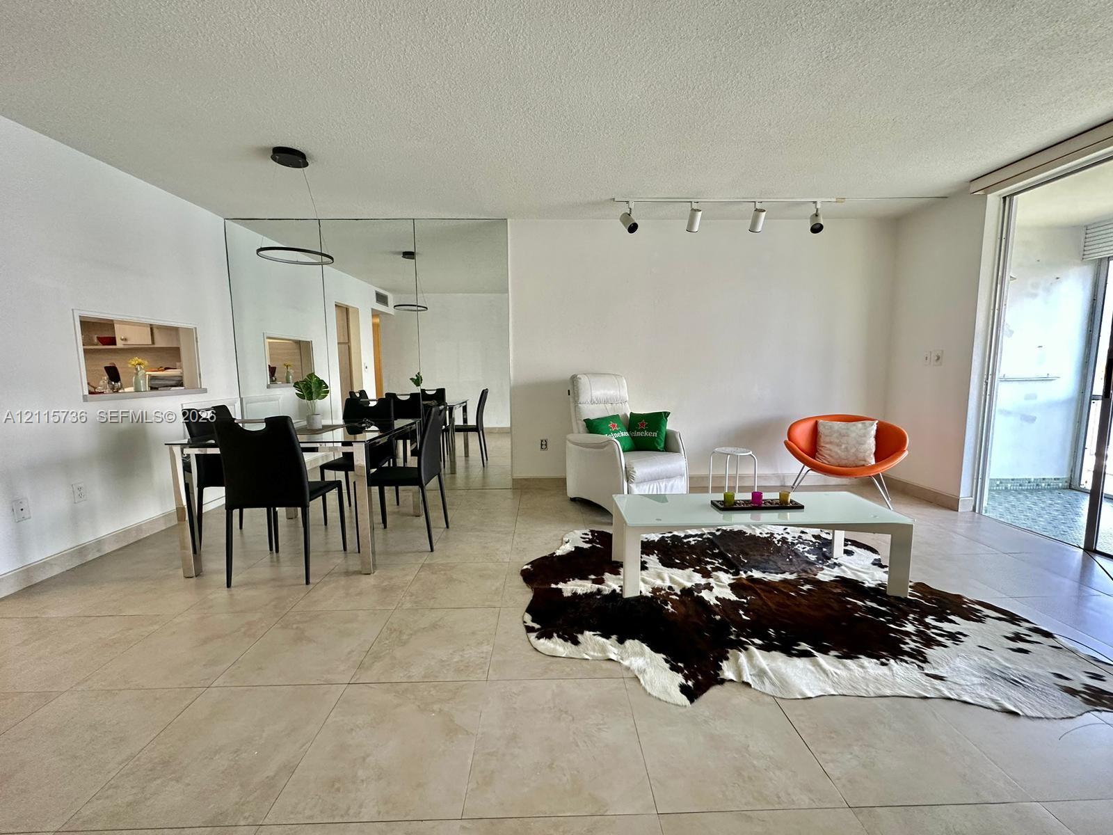 Open-concept interior featuring large-format neutral tile flooring, floor-to-ceiling mirror paneling, track lighting, and a pass-through window