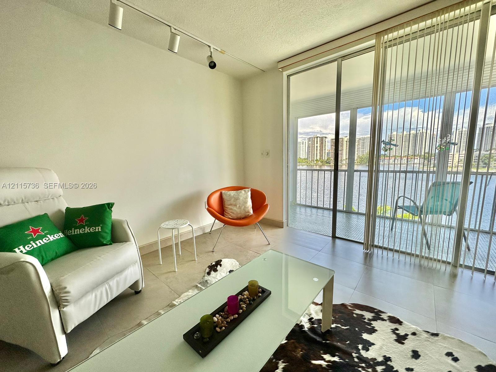 Living area featuring large-format tile flooring, adjustable track lighting, and expansive floor-to-ceiling glass sliding doors opening to a balcony with metal railing