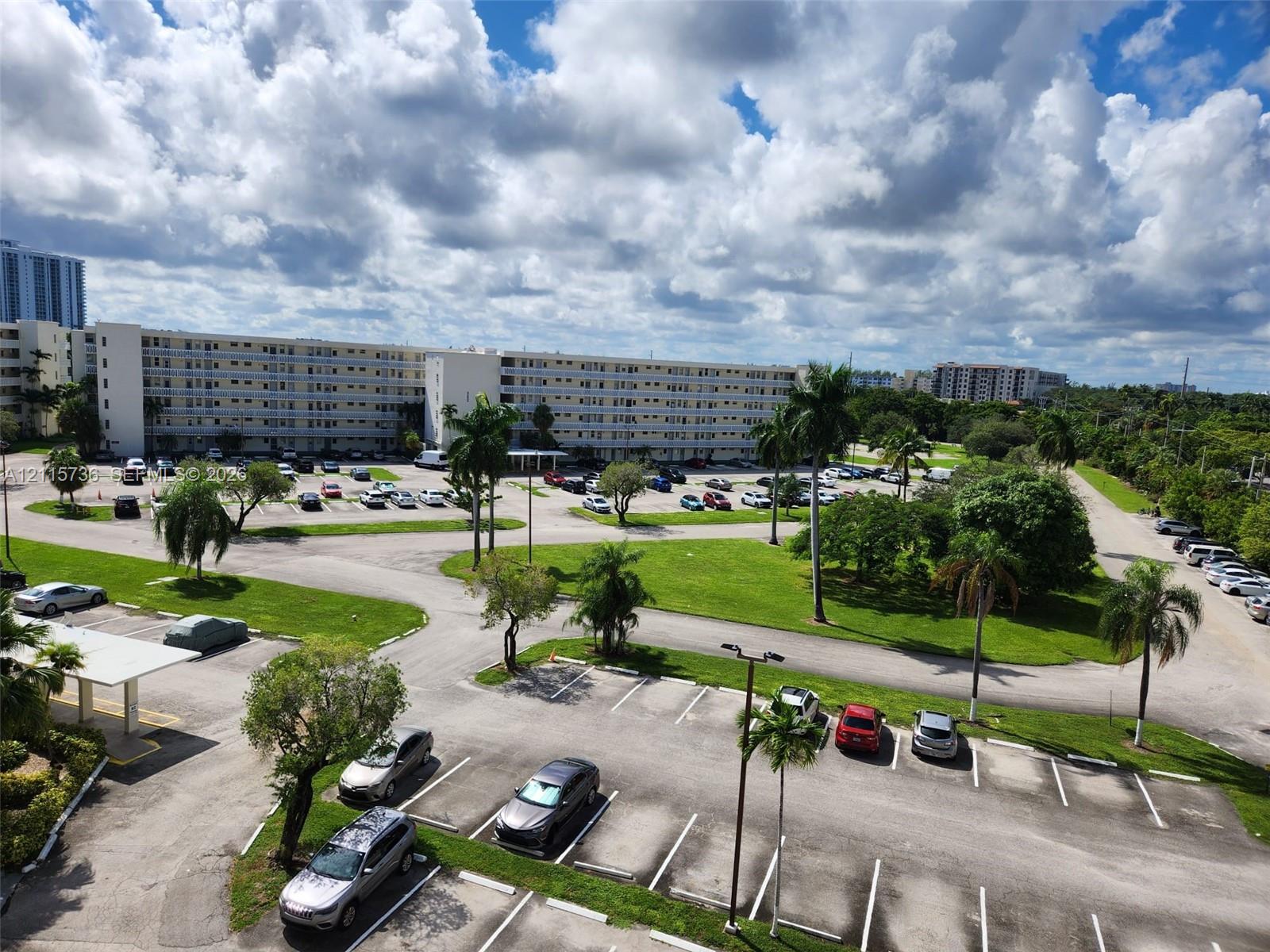 Multi-story residential complex featuring paved surface parking, mature palm trees, and landscaped green spaces