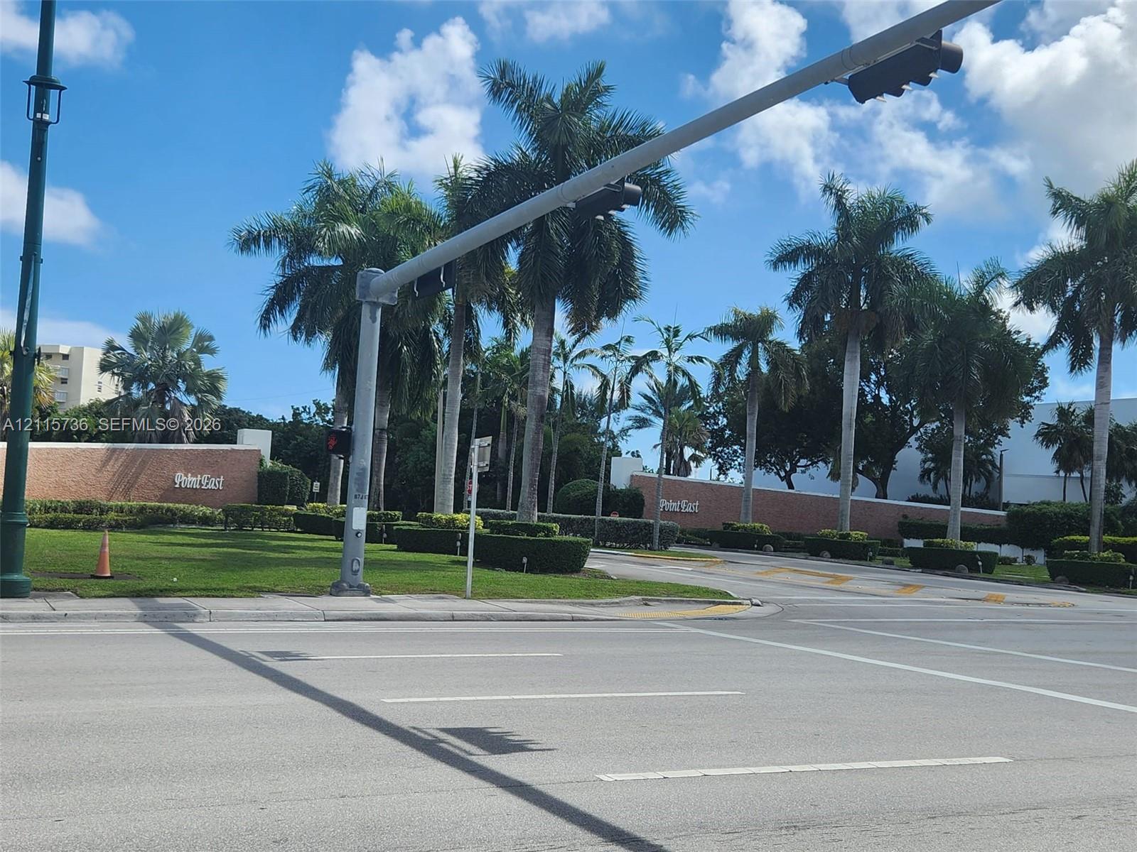 Property entrance featuring brick perimeter walls, manicured landscaping, and mature palm trees