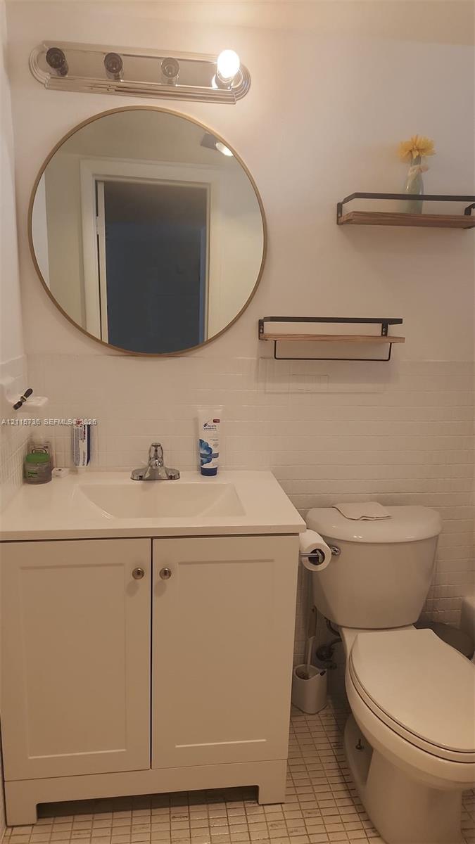 White vanity with integrated rectangular sink, round gold-rimmed mirror, multi-bulb wall-mounted fixture, and dual wall-mounted floating wood shelves