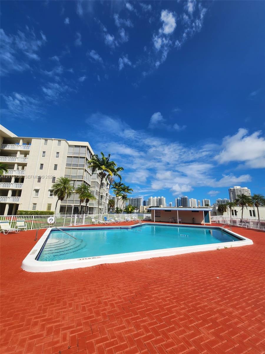 Outdoor swimming pool featuring a herringbone-patterned brick deck, tiered entry steps, and a covered pavilion