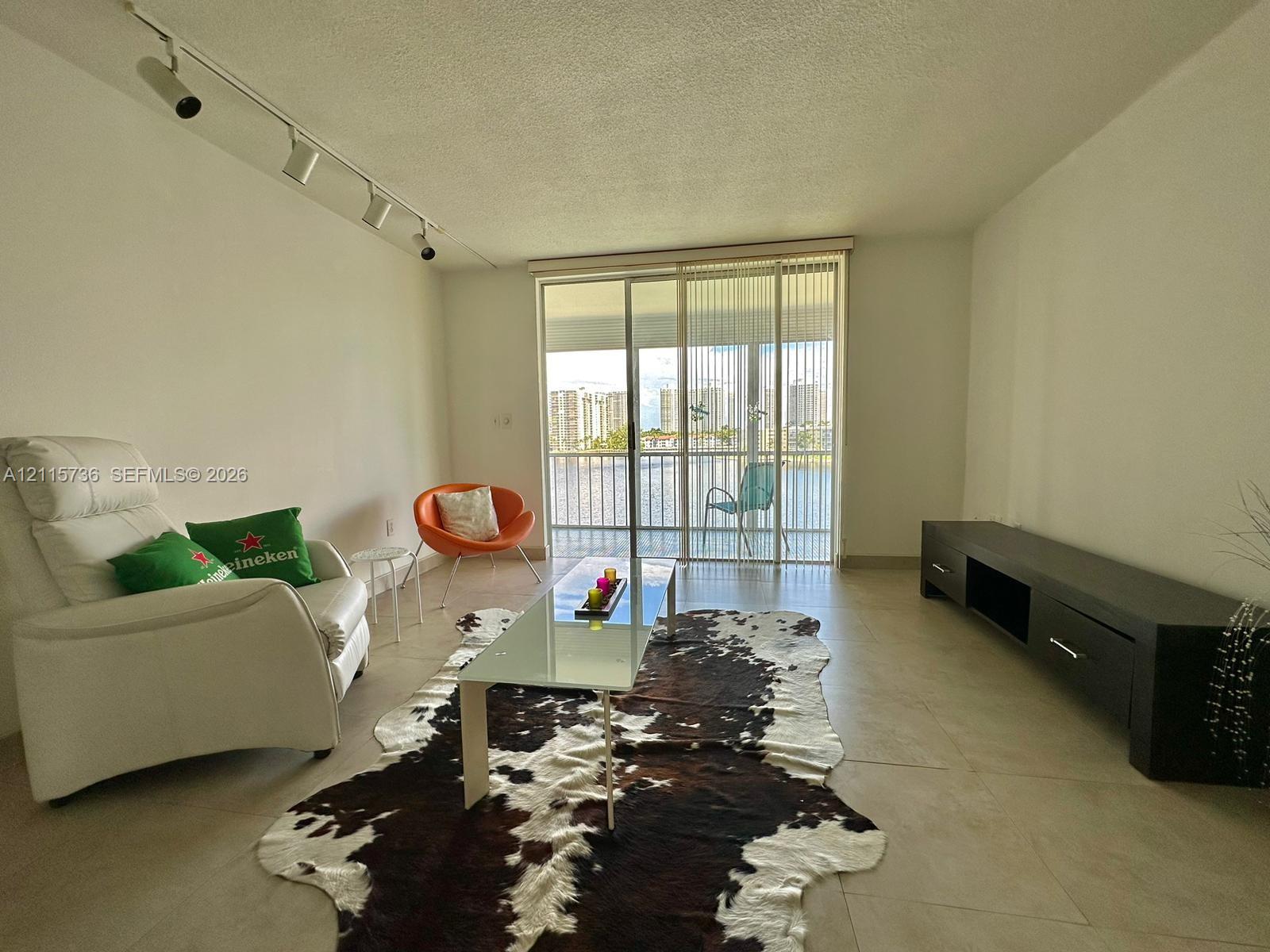 Large-format tile flooring, ceiling-mounted track lighting, and full-height sliding glass doors opening to a private balcony