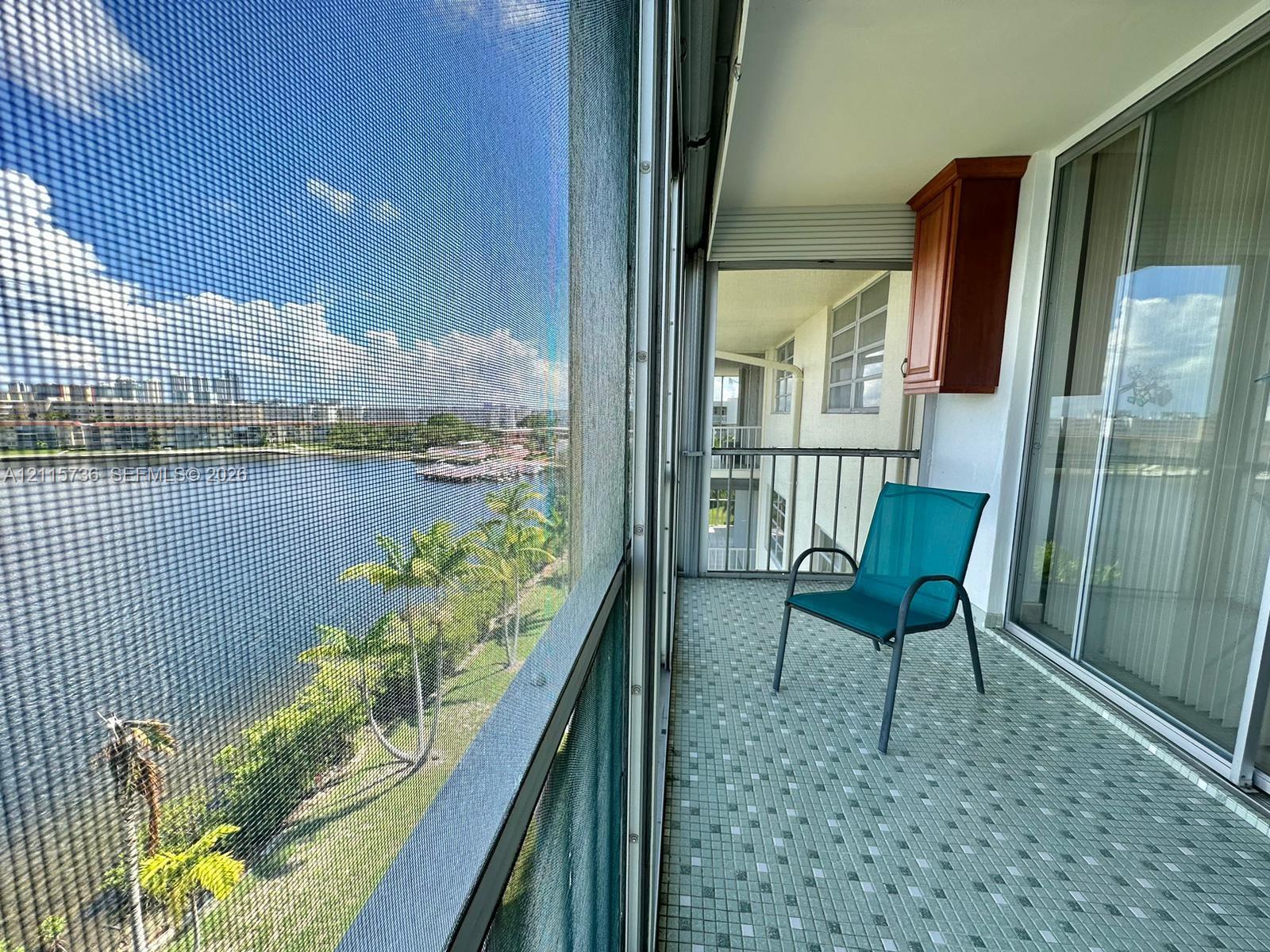 Screened-in balcony featuring tile flooring, a mounted wall cabinet, and metal railings, overlooking a waterfront landscape