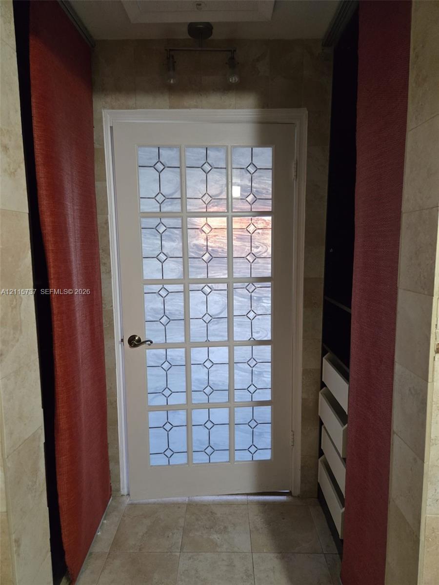 Interior door featuring a multi-pane glass insert with geometric detailing, stone-tiled walls, and built-in cabinetry with white drawer fronts