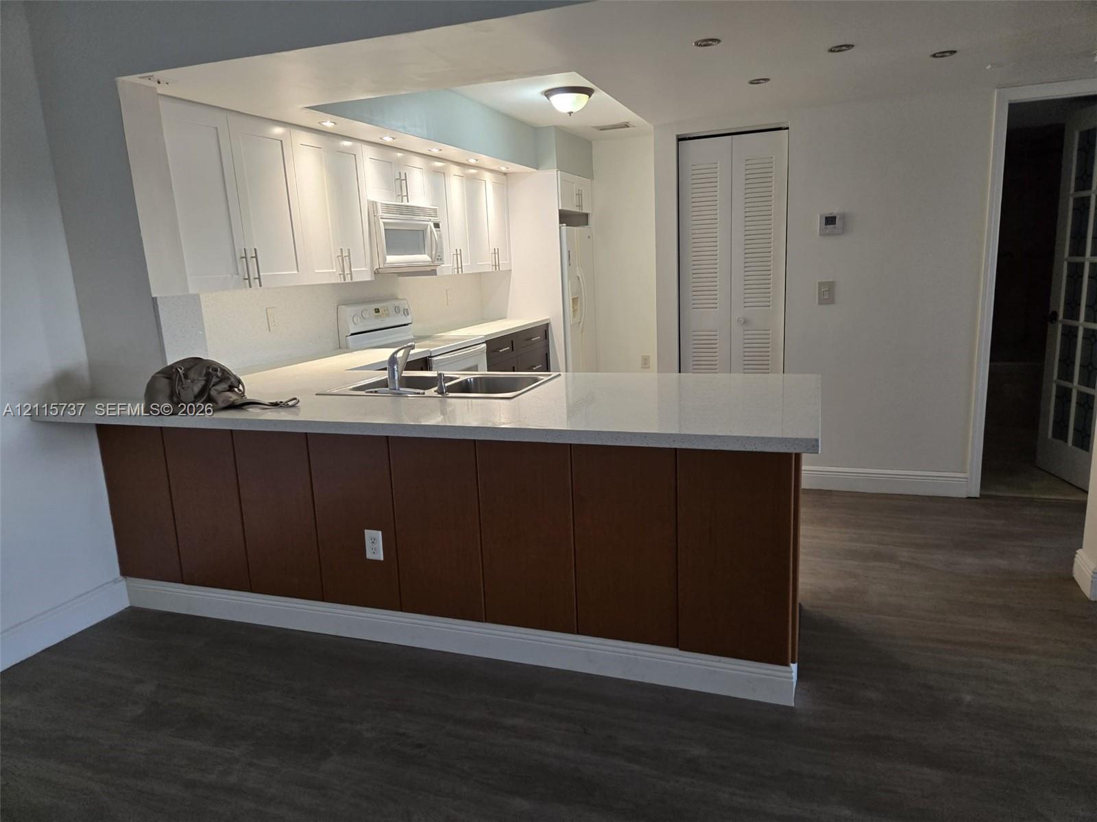 Kitchen featuring white upper cabinetry, contrast lower cabinetry, solid-surface countertops with an integrated breakfast bar, wood-finish flooring, and recessed ceiling lighting