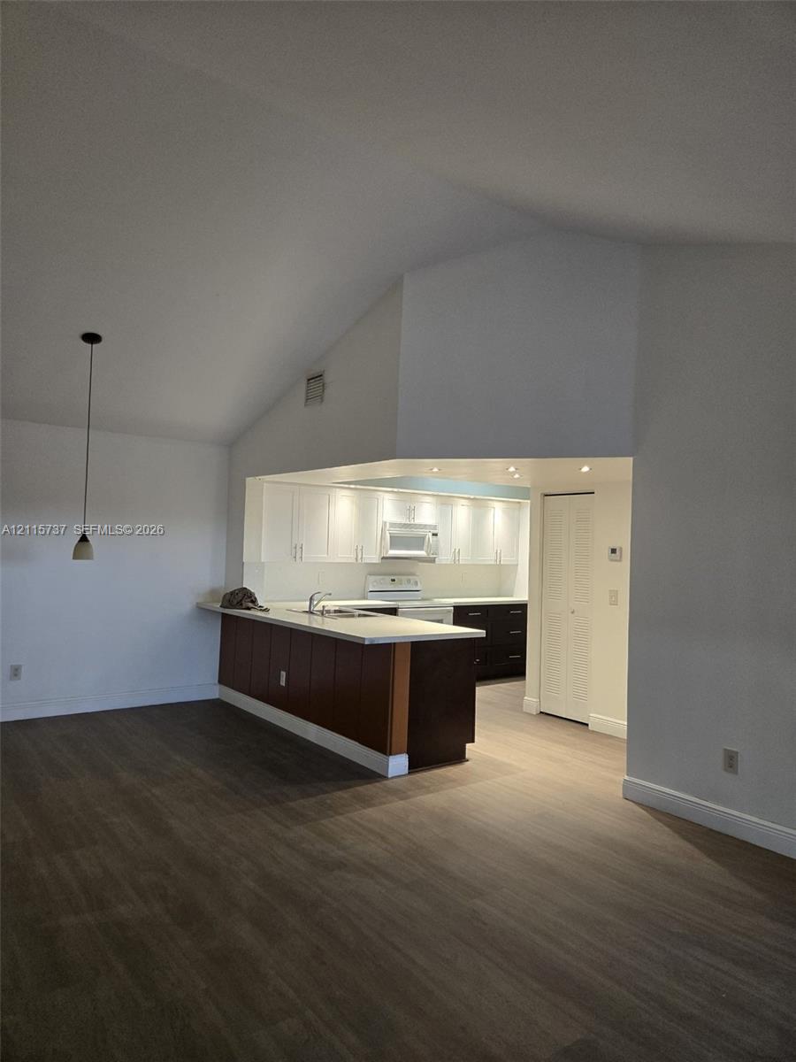 Kitchen featuring wood-finish flooring, vaulted ceilings, white upper cabinetry, a breakfast bar with dark wood-finish cabinetry, and recessed lighting