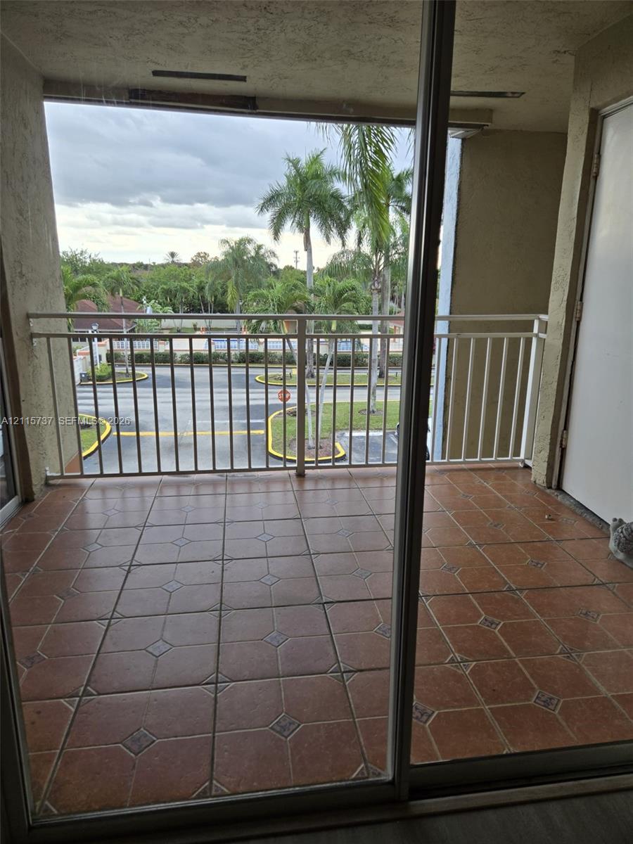 Covered balcony with terra cotta tile flooring, white metal railing, and sliding glass door entry