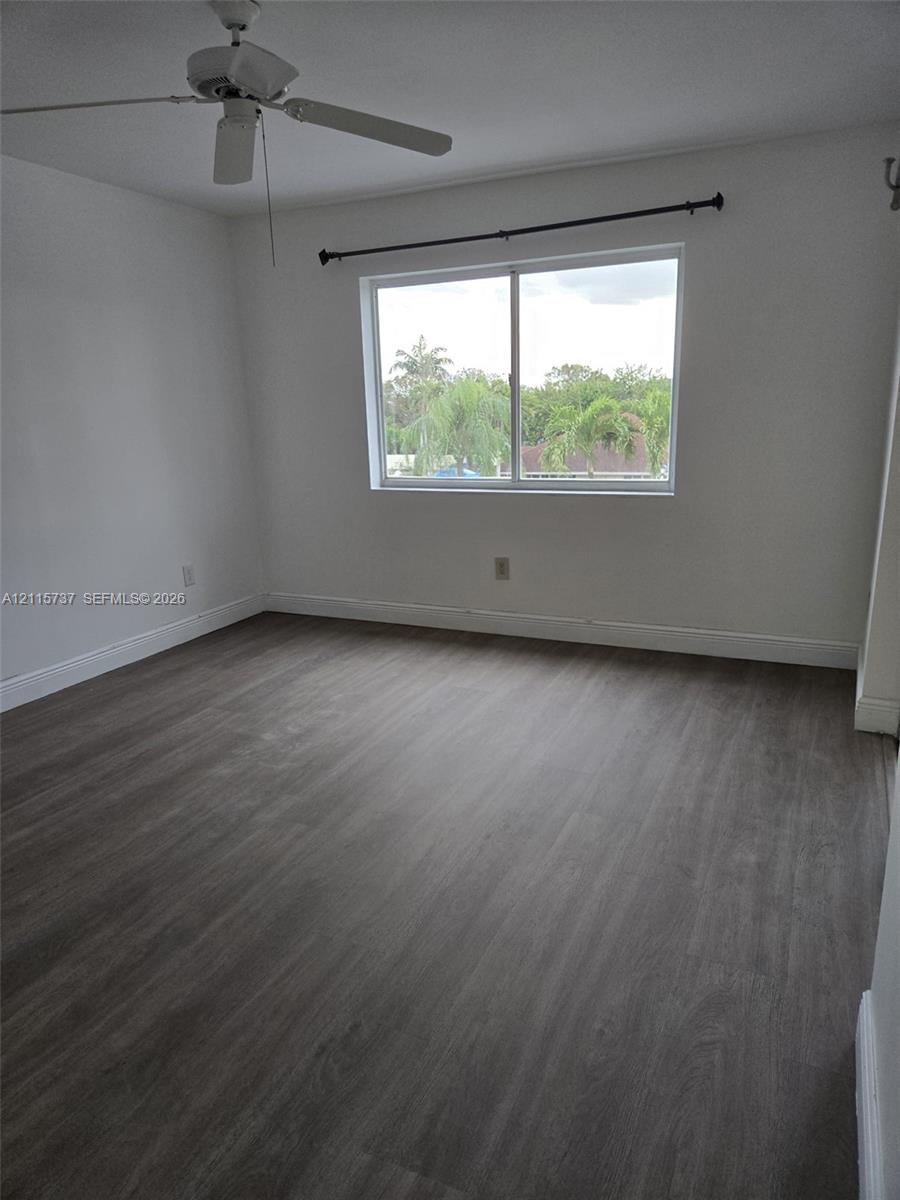 Room featuring wood-finish flooring, a ceiling fan, and a single-pane window with outdoor greenery