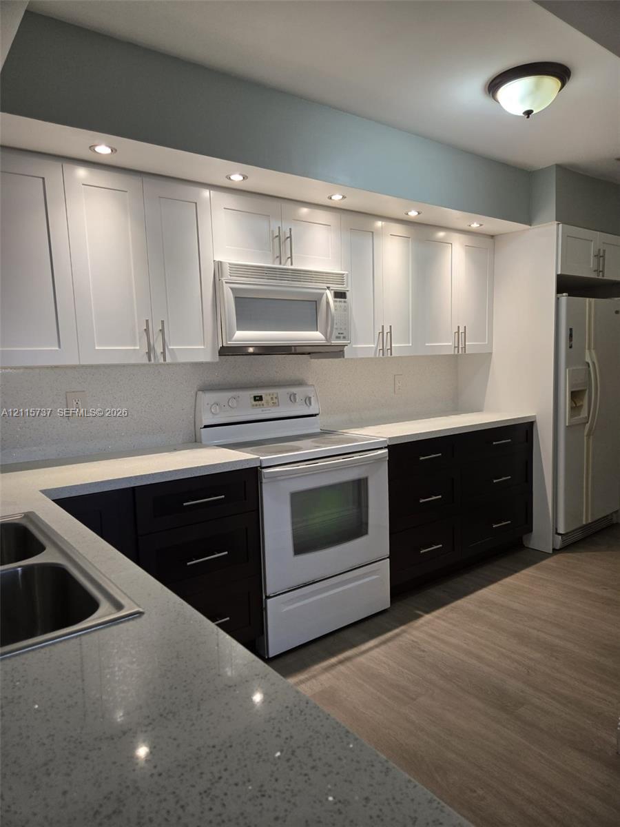 Kitchen featuring two-tone shaker cabinetry, quartz countertops, integrated recessed lighting, wood-finish flooring, and stainless steel sink