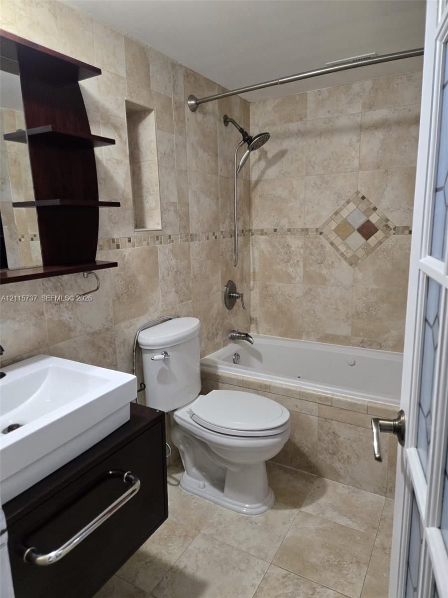 Bathroom featuring a jetted soaking tub, custom tile wall surround with decorative inlay, built-in recessed shelving, floating vanity with vessel sink, and modern polished hardware