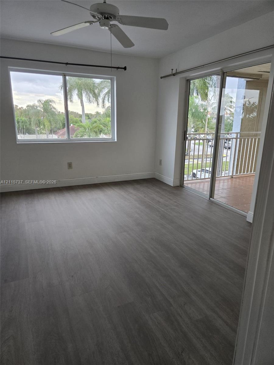 Wood-finish flooring, ceiling fan, single-pane window, and sliding glass door leading to a balcony