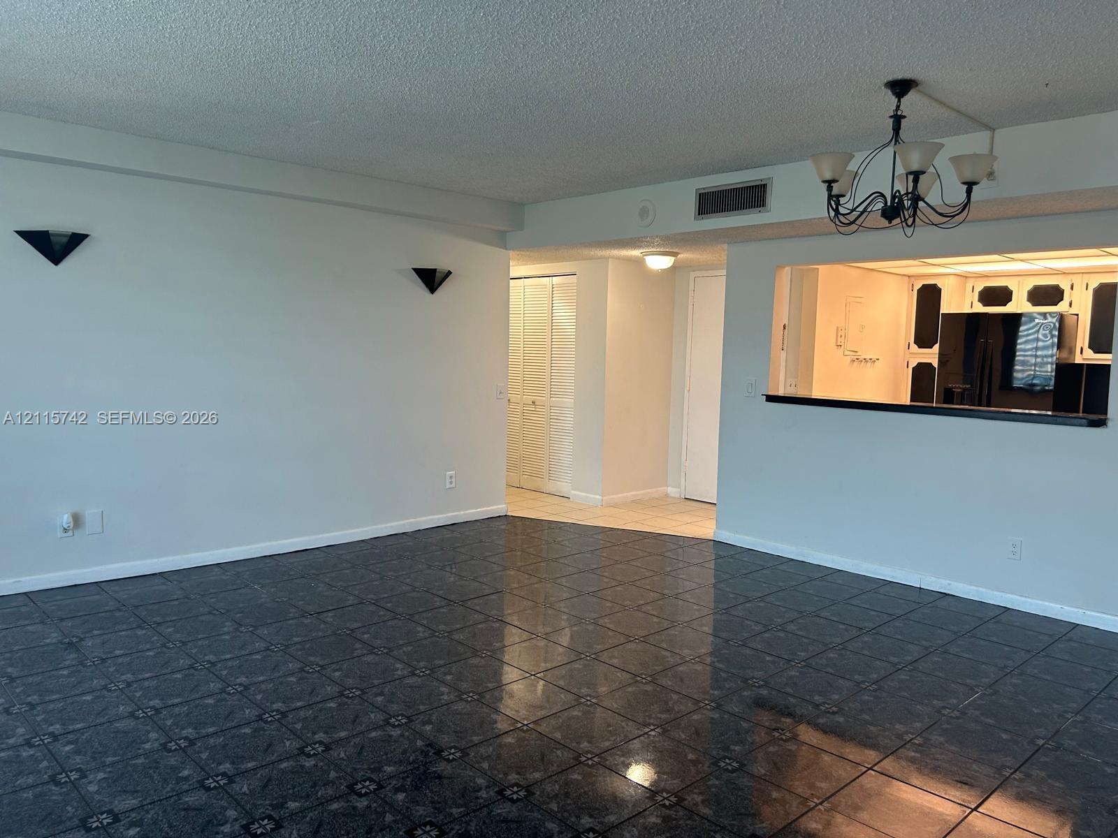 Living area featuring large-format dark floor tile, decorative wall-mounted sconces, a classic chandelier, and an open pass-through window to the kitchen