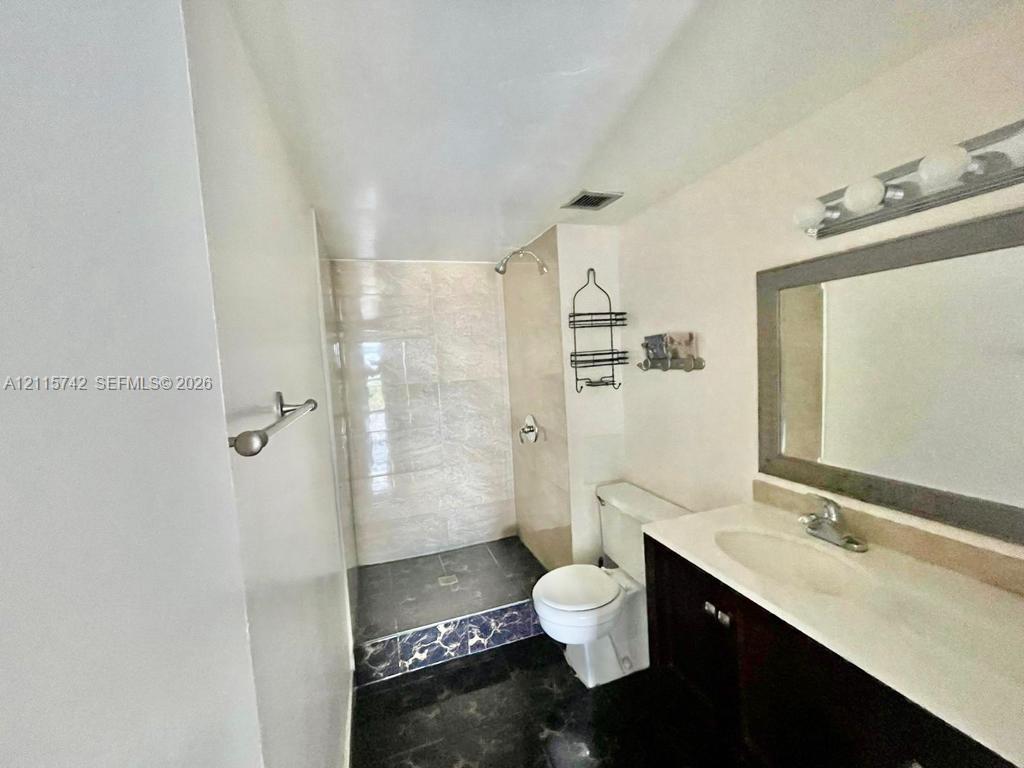 Bathroom featuring a vanity with an integrated basin, a framed wall mirror, a walk-in shower with tiled surround, and dark-toned flooring