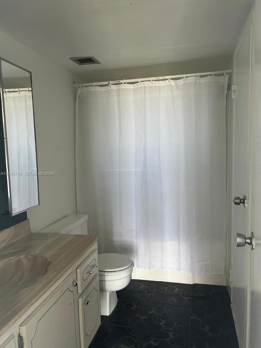 Bathroom featuring a stone-finish countertop, white vanity cabinetry with metal hardware, a wall-mounted mirror, and tile flooring