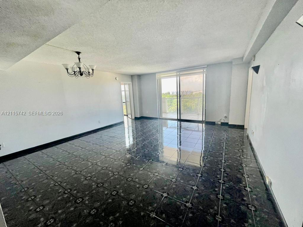 Open-concept living space featuring high-gloss decorative tile flooring, multi-arm metal chandelier, and floor-to-ceiling sliding glass doors opening to a private balcony